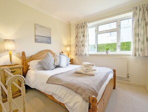 Een netjes ingerichte slaapkamer met een houten bed, wit beddengoed, een bedlampje, een raam met gordijnen en een radiator.