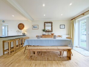 Een eetgedeelte met een houten tafel, bankjes, een klok en een spiegel aan de muur.