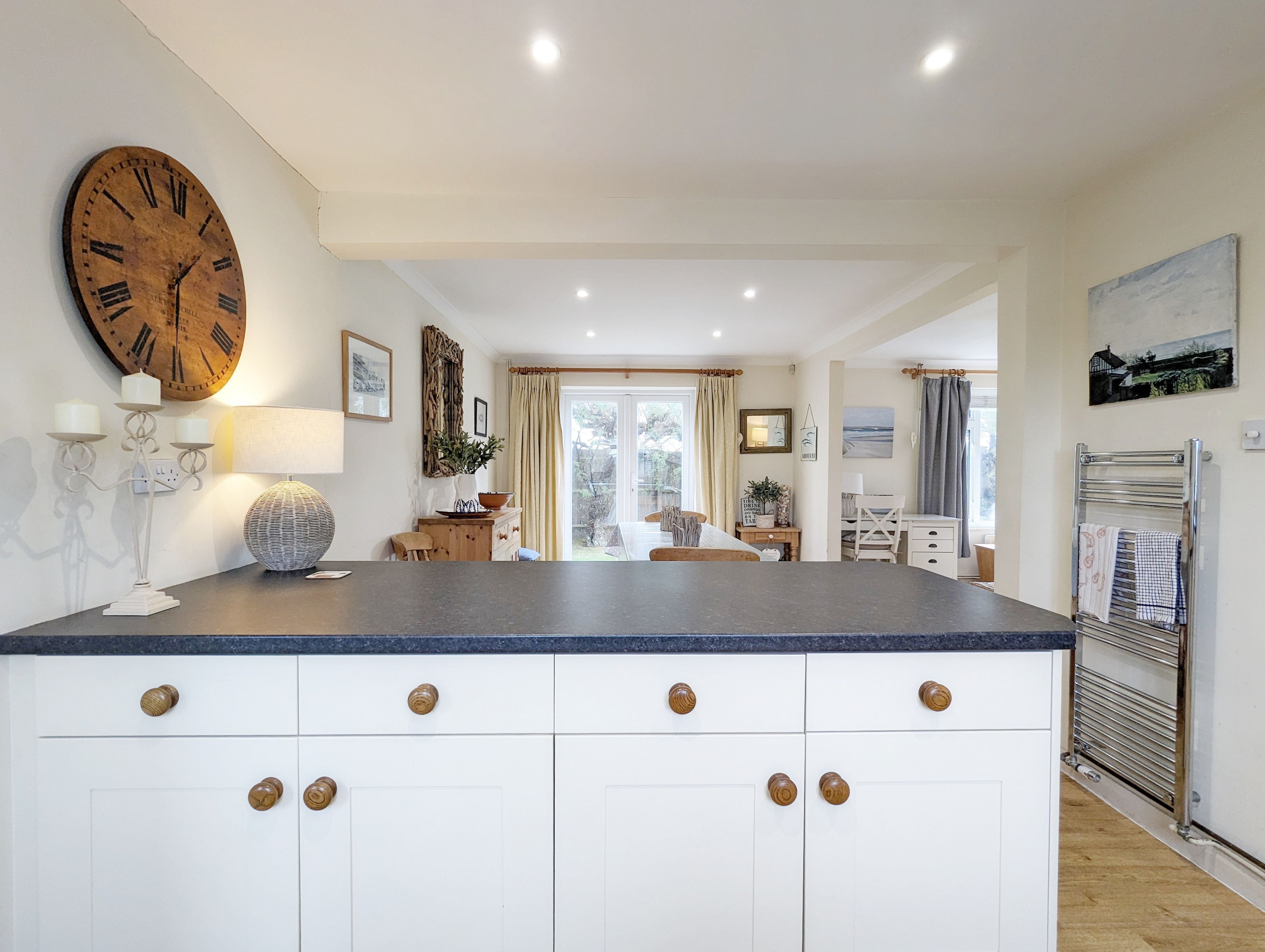 A spacious kitchen with a large island, white cabinetry, and a rustic wooden clock.
