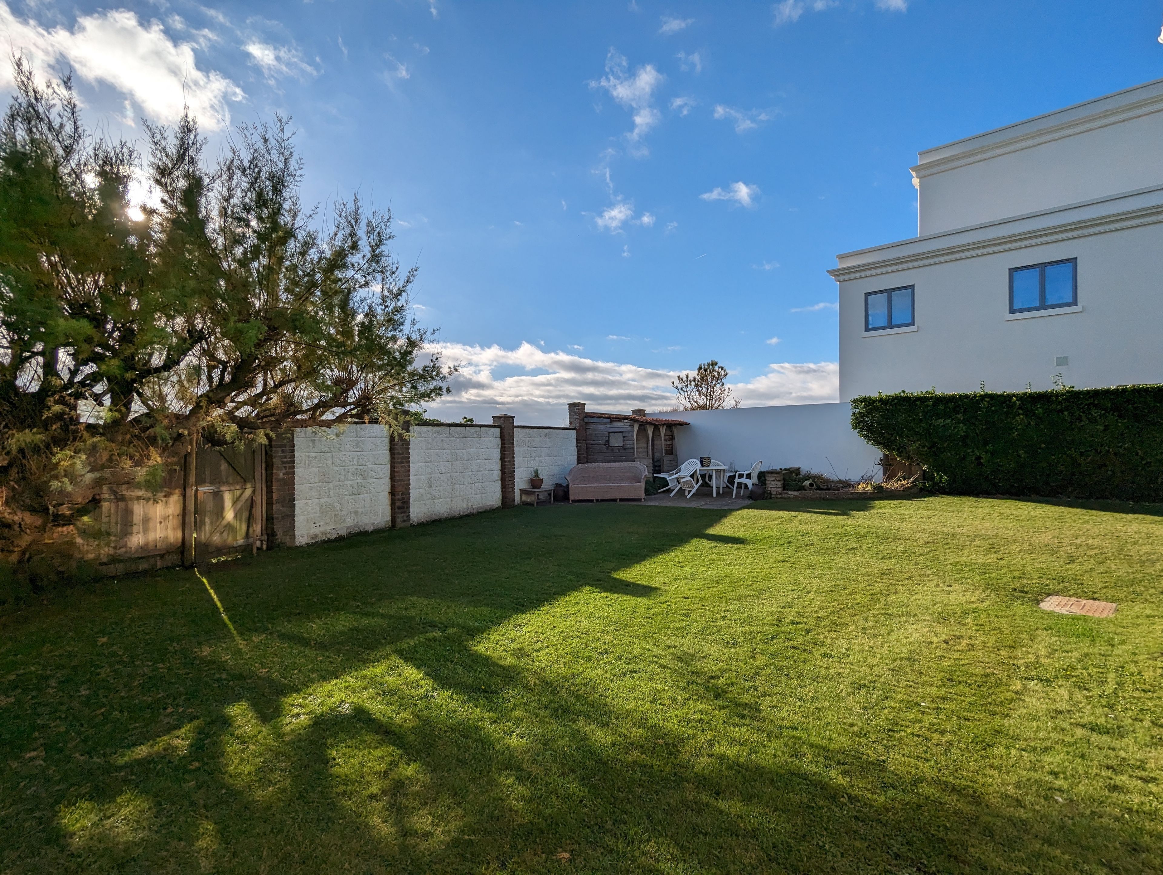 A well-maintained backyard with a grassy lawn, a wooden fence, and a white building with a chimney.