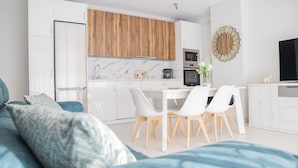 Eine moderne Küche mit weißen Schränken, Holz-Oberschränken und einem Essbereich mit weißen Stühlen und einem Tisch.