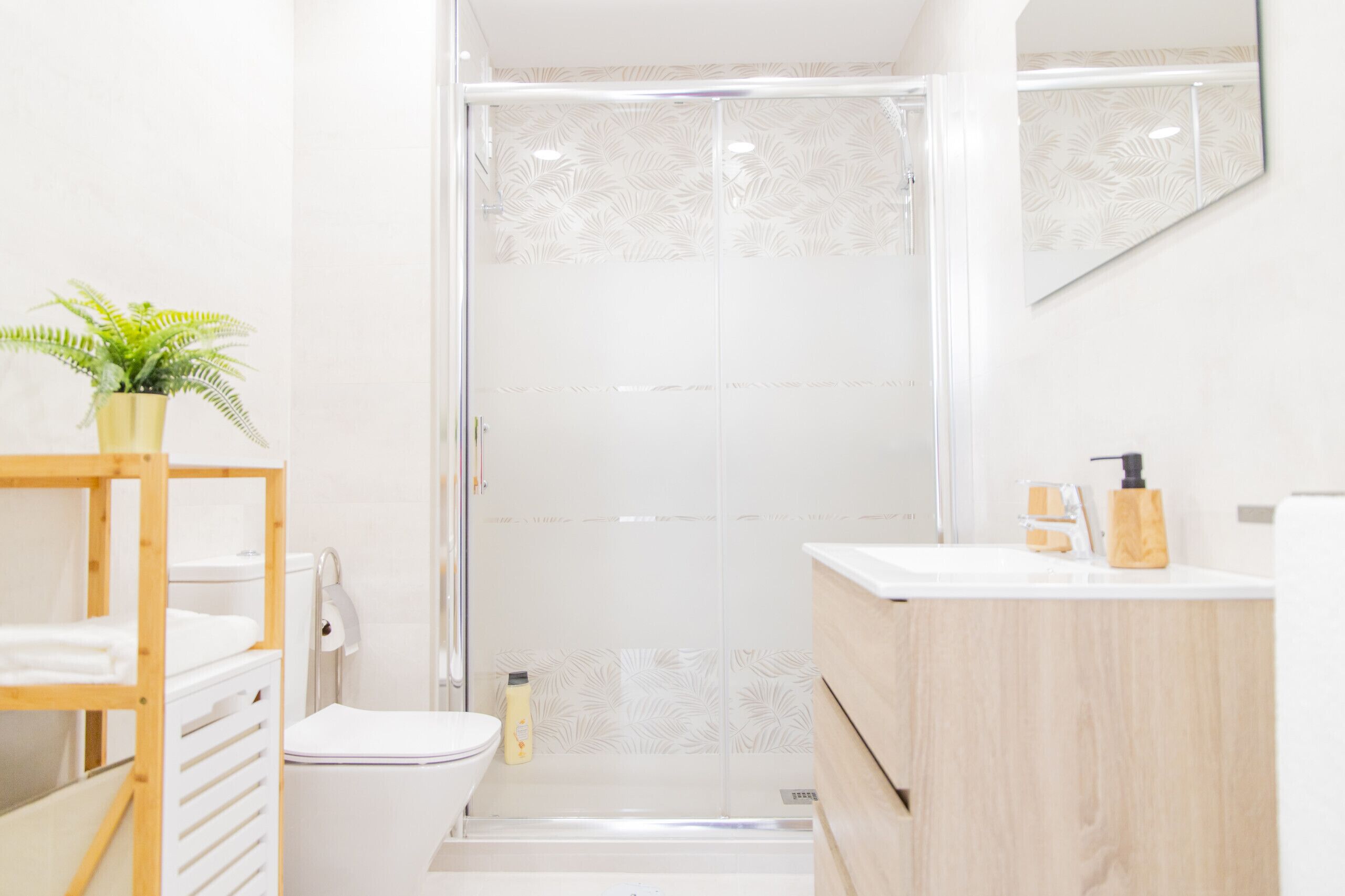 A modern bathroom with a glass-enclosed shower, a wooden vanity, and a potted plant.