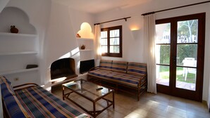 Ein Wohnzimmer mit einer Couch, einem Glastisch, einem Kamin und einem großen Fenster mit Vorhängen.