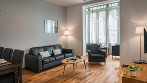 A modern living room with a dark leather sofa, a wooden coffee table, and a dining area with a dark wooden table and chairs. - Alibei 1 - Habitat Apartments (Barcelona)