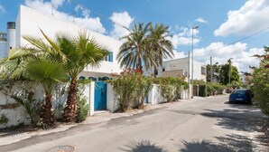 A quiet residential street with white houses, palm trees, and a parked car.