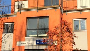Un edificio con un letrero de centro de servicios, ventanas grandes y un árbol en la fachada.