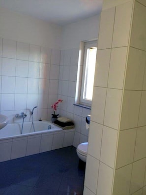 Une salle de bain avec une baignoire, des toilettes et une fenêtre.