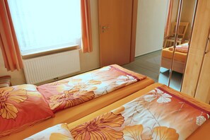 Une chambre avec deux lits, une armoire en bois, un radiateur et une fenêtre avec des rideaux.