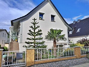 Ett tvåvåningshus med vit fasad, en sockel av tegel och ett staket av metall.