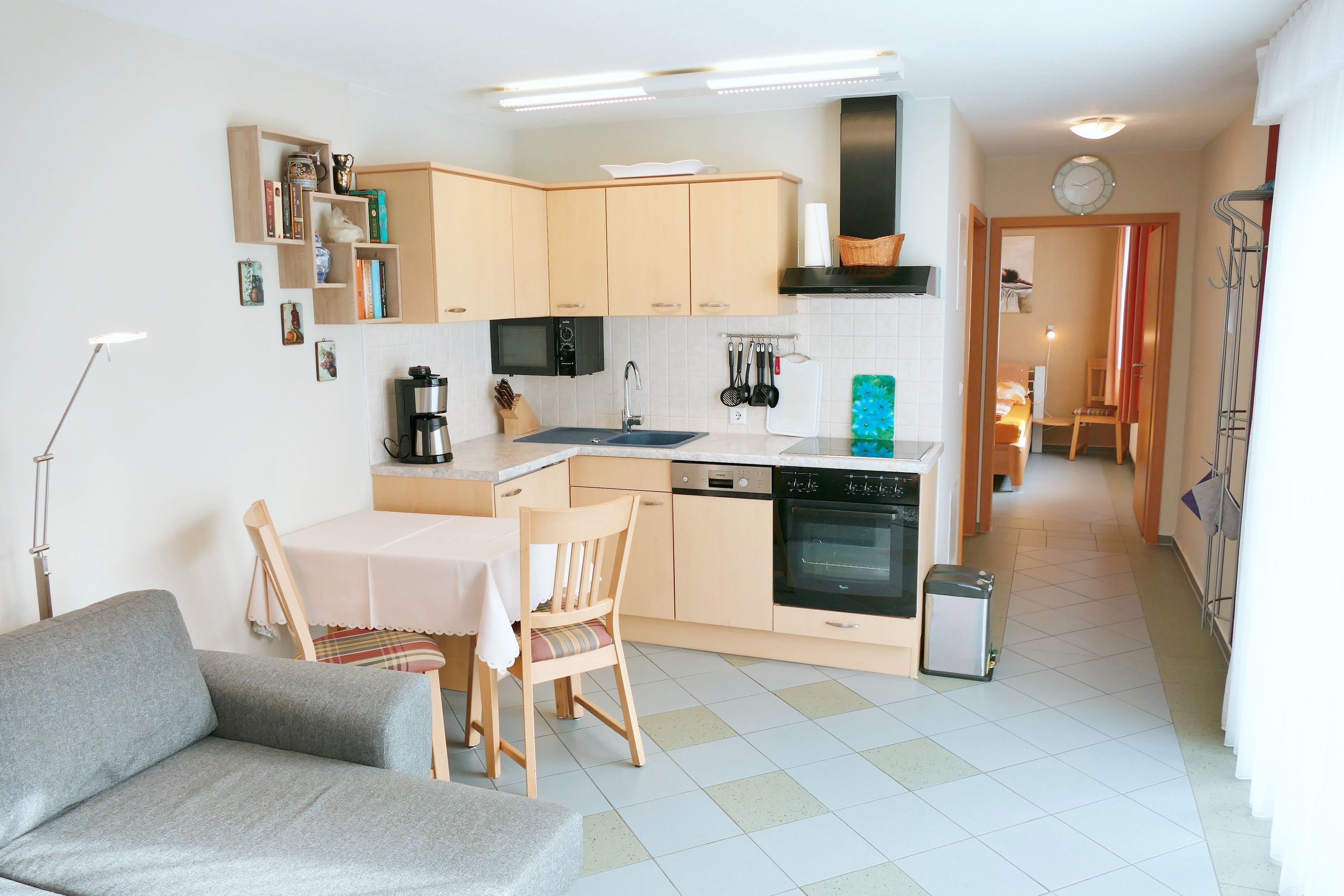 Ett kompakt kök med träskåp, en matplats med bord och stolar samt en liten papperskorg.