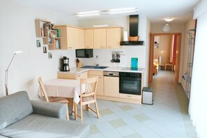 Ett kompakt kök med träskåp, en matplats med bord och stolar samt en liten papperskorg.