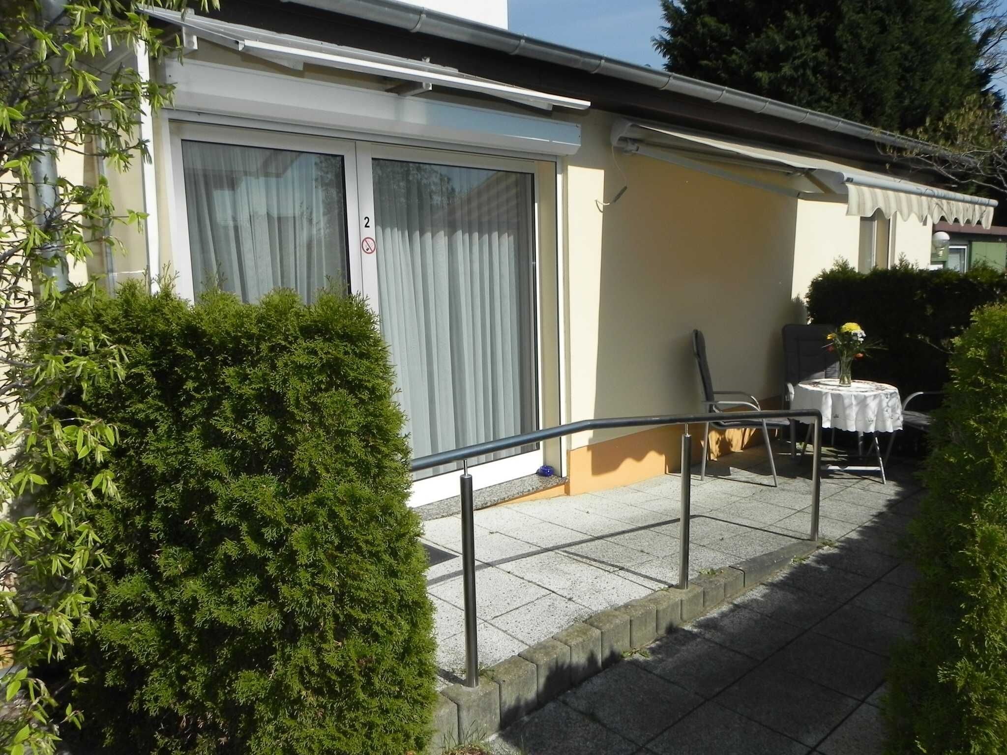 Un immeuble résidentiel doté d’une porte-fenêtre coulissante, d’un petit patio avec une table et des chaises, et d’une plaque portant le numéro « 2 » sur la porte.