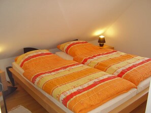 A single bed with a striped blanket and two pillows, a bedside lamp, and a wooden nightstand. - Vacation apartment in Nessmersiel 20-041a - 200-041a (Dornum)
