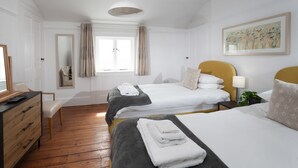 Quarto de hotel com duas camas, uma escrivaninha, uma cadeira, uma janela com cortinas, um quadro na parede e um lustre.