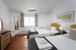 Hotellihuone, jossa on kaksi sänkyä, työpöytä, tuoli, ikkuna, jossa on verhot, taulu seinällä ja riippuvalaisin.
