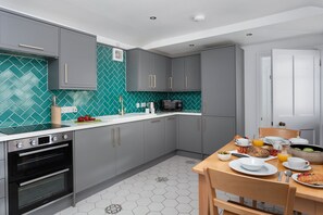 A modern kitchen with grey cabinets, a white countertop, and a green tiled backsplash.