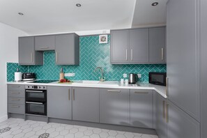 A modern kitchen with grey cabinets, a white countertop, and a herringbone tile backsplash.