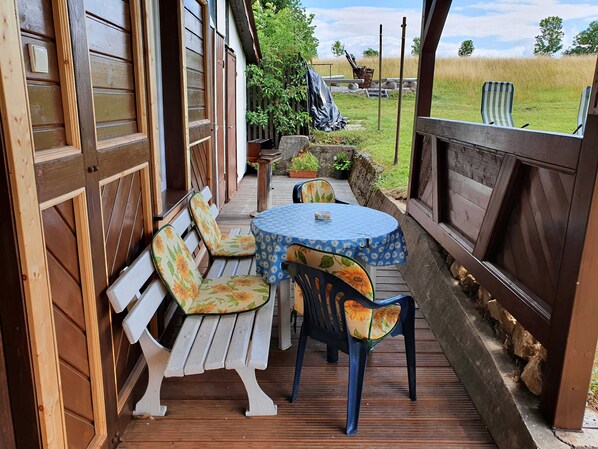A wooden deck with a table and chairs, a bench, and a view of a grassy field.