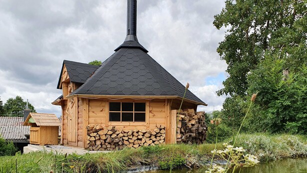 Una cabaña de madera con techo hexagonal, una chimenea y un ventanal.