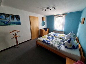 A bedroom with a bed, a wooden wardrobe, a mirror, a picture on the wall, and a window with curtains.