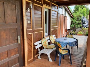 A wooden door with a latch, a bench, a table with a floral tablecloth, and potted plants in a garden area.
