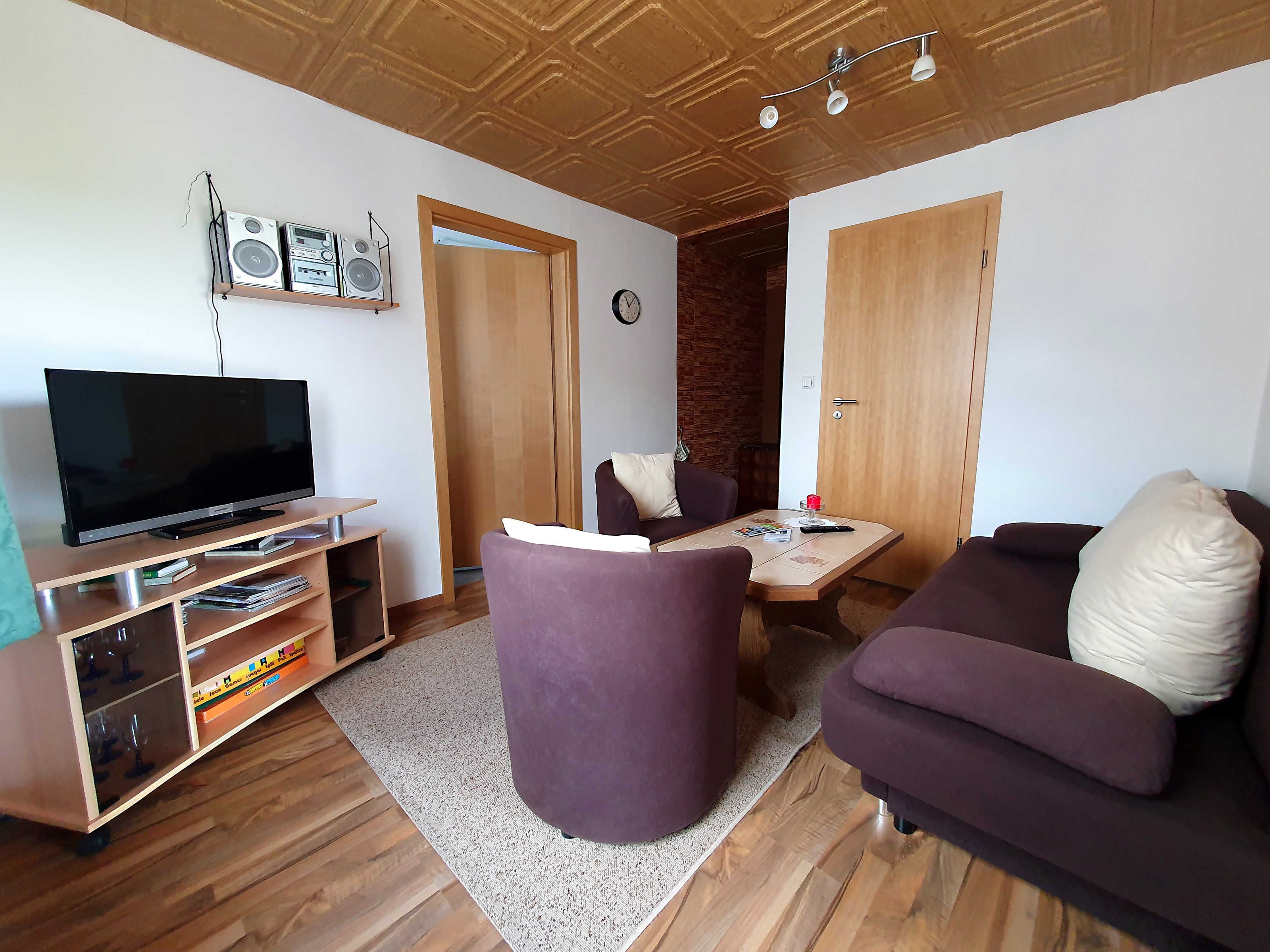 Ein Wohnzimmer mit Fernseher, Lautsprechern, einer Couch, einem Couchtisch und einer Holzbalkendecke.
