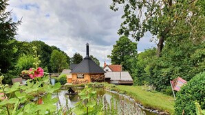 Una cabaña rústica con chimenea, un estanque y abundante vegetación.
