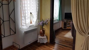 Una habitación con piso de madera, un radiador, una mesita con un florero, un televisor y un armario.