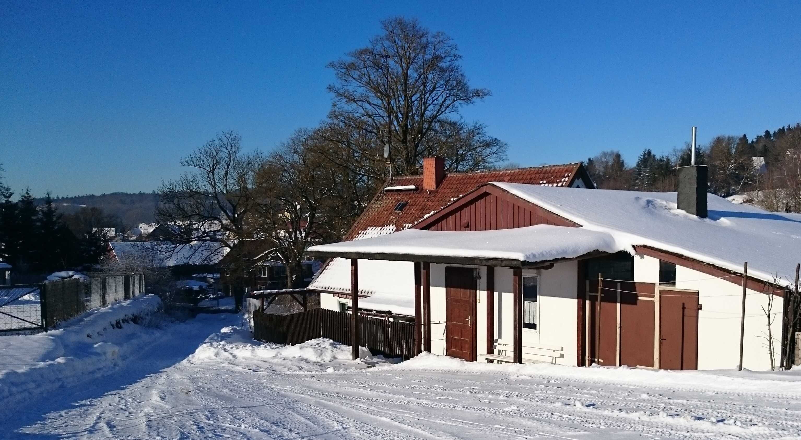 Un edificio imbiancato dalla neve con tetto rosso, una recinzione in legno e un cielo azzurro intenso.