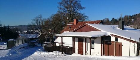 Un edificio imbiancato dalla neve con tetto rosso, una recinzione in legno e un cielo azzurro intenso.