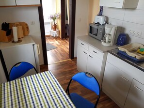 Una kitchenette compacta con microondas, cafetera y un pequeño comedor con mantel a cuadros.