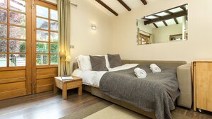 Un dormitorio con una cama grande, suelo de madera, una mesita de noche, una lámpara, un espejo y vistas por una ventana.