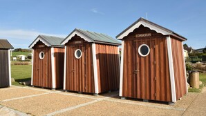 Three wooden portable toilets with white trim and a peaked roof, labeled "PETREL," "GREBE," and "CORMORAN."