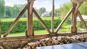 A rustic wooden structure with a view of a green landscape and a stone building in the distance.