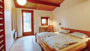 Une chambre à coucher avec un lit en bois, un bureau avec une chaise, une fenêtre et une porte donnant sur l’extérieur.