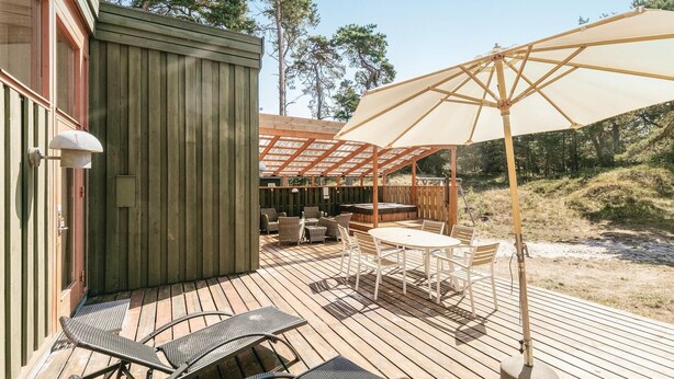Une terrasse en bois, aménagée avec du mobilier d’extérieur, notamment une table et des chaises, et un grand parasol pour créer de l’ombre.