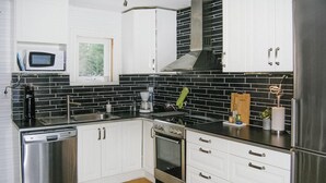 Une cuisine moderne avec des meubles blancs, un dosseret en carreaux noirs, des appareils en acier inoxydable et une fenêtre au-dessus de l’évier.
