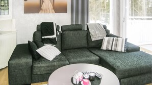 Un salon moderne avec un canapé d’angle, une table basse ornée de bougies et une grande fenêtre donnant sur un paysage arboré.
