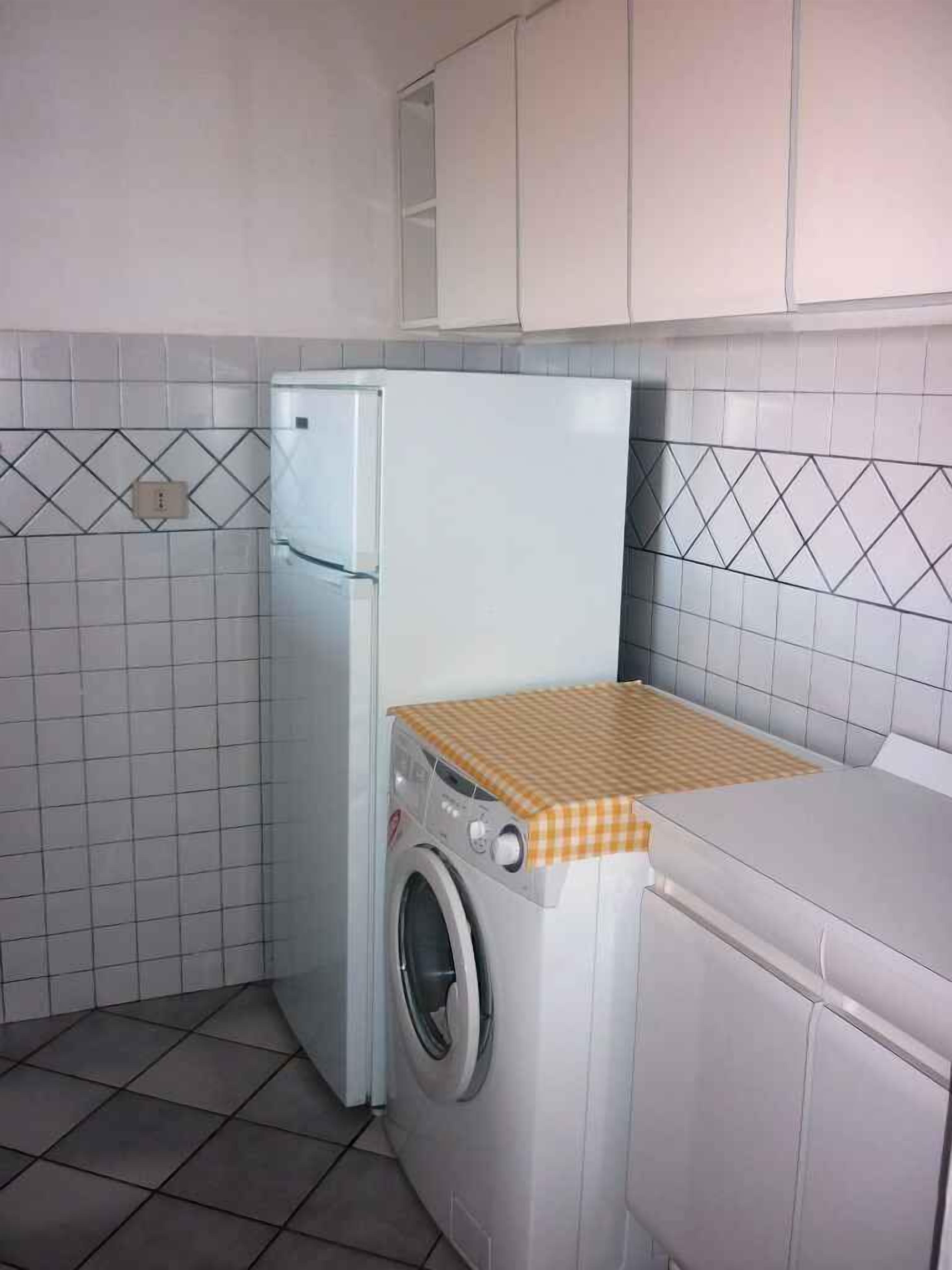 Cocina compacta con refrigerador, lavadora y salpicadero de azulejos.