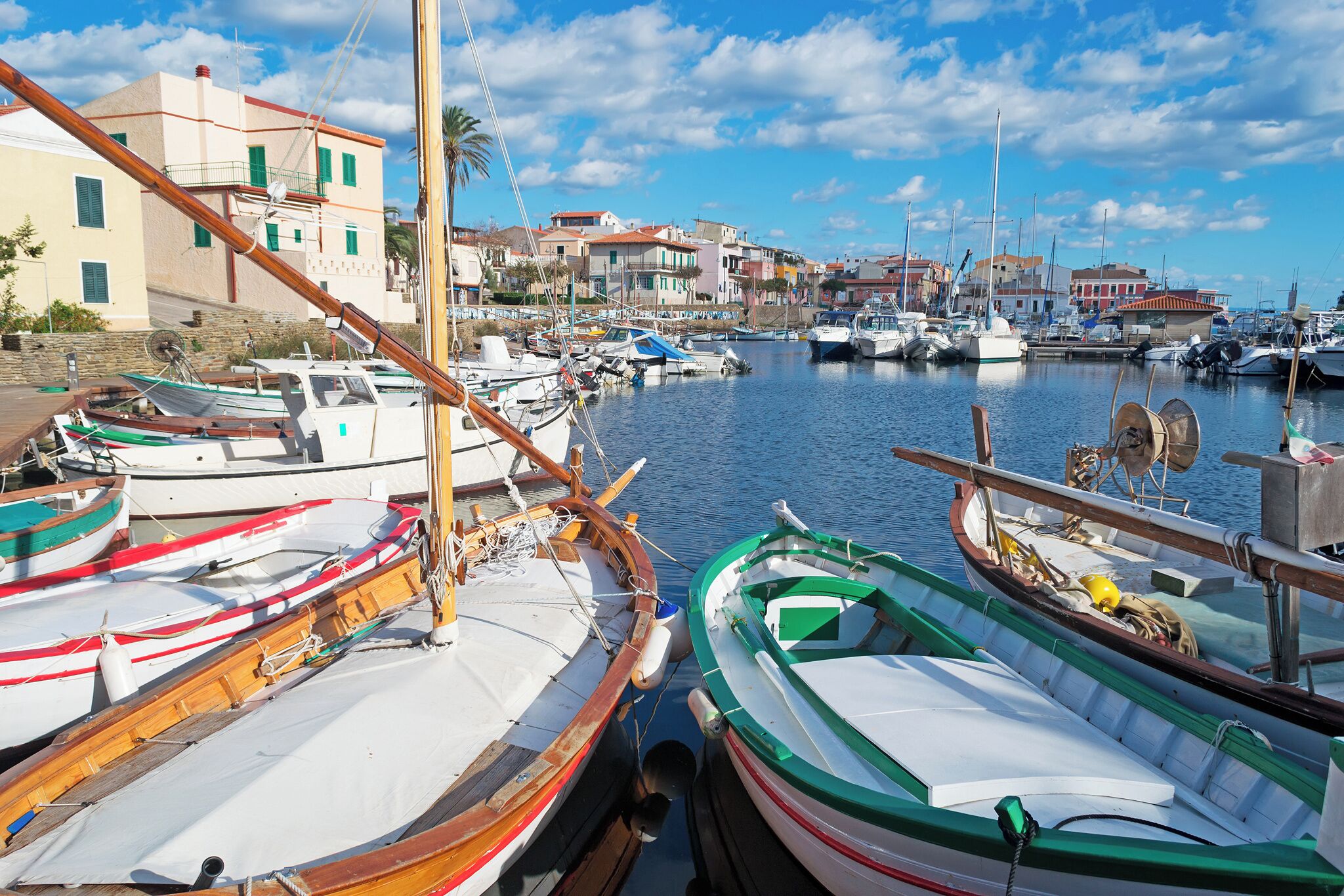 A marina with boats docked, buildings in the background, and a clear sky.
