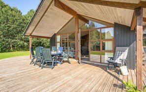 A wooden deck with a covered seating area, large windows, and a view of a green landscape. - Beautiful home in Ansager with sauna (Ansager)