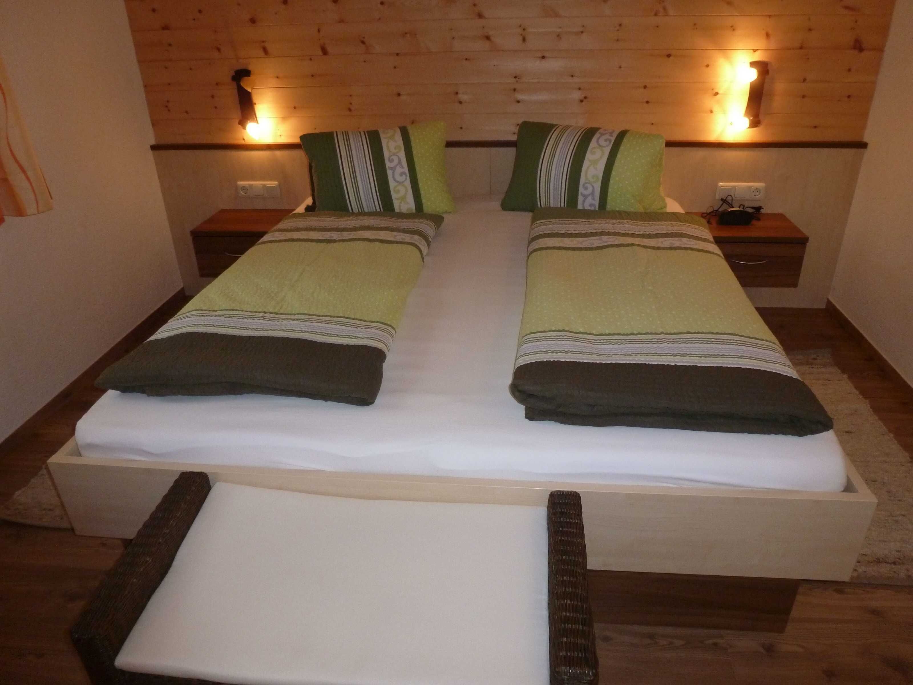 A double bed with two pillows, a wooden headboard, bedside lamps, and a nightstand.