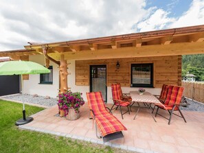 A wooden cabin with a covered patio, outdoor seating, and a flower pot.