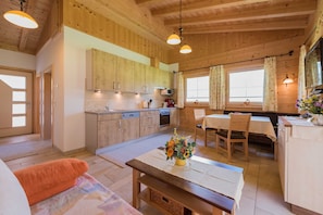 A wooden interior with a kitchen, dining area, and a sofa with an orange cushion.