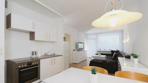 A modern kitchen with a built-in oven, a dining area with a white table and chairs, and a living area with a sofa and a TV. - 2 bedroom cozy apartment in Goslar (Goslar)