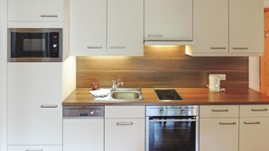 Una cocina moderna con armarios blancos, electrodomésticos de acero inoxidable, incluyendo un microondas, lavavajillas y horno, una encimera de madera y un lavaplatos empotrado.