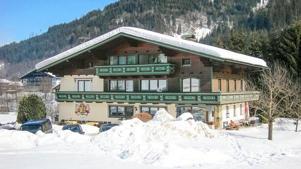 Un edificio de estilo chalé con techo inclinado, varios balcones y montañas al fondo.