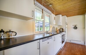 A modern kitchen with white cabinetry, a black countertop, and a wooden ceiling. - 2 bedroom amazing home in Grenaa (Grenaa)