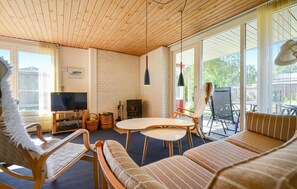 A cozy living room with a fireplace, a television, and a large window offering a view of the outdoors. - 2 bedroom amazing home in Grenaa (Grenaa)