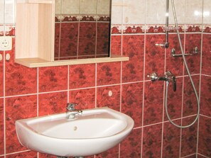 Een badkamer met een wit wastafelmeubel, een spiegel erboven en een douche met een handdouche.